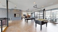 Located at 3001 S 21st Ave in Bozeman, Montana, this expansive single-floor amenity space offers a thoughtfully designed environment built for recreation, collaboration, and productivity. The generously sized layout spans a substantial footprint and encompasses several distinct functional zones, each finished with a cohesive modern aesthetic.

The centerpiece game room commands immediate attention, featuring a full-sized pool table and foosball table set atop polished concrete floors. A defining architectural feature is the oversized glass-panel overhead door that opens fully to an adjacent outdoor terrace, blurring the boundary between interior and exterior and flooding the space with natural light.

Adjacent to the game room, a well-appointed wet bar and lounge area includes a large island with bar seating, warm wood cabinetry, a terracotta tile backsplash, built-in appliances, and a wall-mounted display screen — ideal for gatherings and events.

A multi-level lobby and lounge area showcases soaring double-height ceilings, floor-to-ceiling windows, sleek cable-rail mezzanine balustrades, and a dramatic pendant chandelier, creating an impressive sense of verticality and openness.

The co-working zone offers a central island with seating alongside frosted-glass private office enclosures, providing both collaborative and focused work settings. Individual private offices feature natural light, custom wood desks, and curated artwork, completing this well-rounded community space.