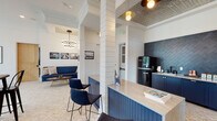 Located at 5010 W Broad St in Sugar Hill, Georgia, this thoughtfully designed single-floor commercial space blends modern farmhouse aesthetics with contemporary touches. Herringbone-patterned brick flooring runs throughout, anchoring the open layout and lending warmth to the bright, airy interior. Soaring ceilings and large floor-to-ceiling windows flood the space with natural light and offer views of the surrounding streetscape and an adjoining outdoor patio area.

Structural columns clad in shiplap paneling define distinct zones within the open floor plan. A welcoming lounge nook features a built-in navy sectional sofa, an oval wood coffee table, and a striking sputnik-style chandelier overhead, with patterned wallpaper adding visual interest to the accent wall. Curated black-and-white framed artwork enhances the sophisticated atmosphere throughout.

A functional kitchenette is outfitted with navy blue cabinetry, a marble-look countertop, a matte black retro refrigerator, and a bold herringbone-tiled backsplash in deep blue. A decorative tin-panel ceiling detail crowns this area. Additional seating includes high-top bar tables with metal bistro chairs and casual dining tables with mixed seating, making this space well-suited for gathering, collaboration, or community engagement.