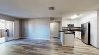 Located at 2450 Hilton Head Pl in El Cajon, California, this single-floor residence offers a clean, modern aesthetic throughout. The open-concept living area is finished with wood-look luxury vinyl plank flooring and neutral gray walls, creating a bright and welcoming atmosphere. A sliding glass door and front entry door with a window panel bring in natural light and provide outdoor access. The kitchen is well-appointed with white shaker-style cabinetry, dark countertops, a stainless steel sink, and a full suite of stainless steel appliances including a refrigerator, electric range, and over-the-range microwave. A peninsula counter separates the kitchen from the living space, offering a functional layout. The bedrooms feature plush wall-to-wall carpeting and neutral tones, with windows that frame views of the surrounding greenery, filling each room with natural light. The bathroom is finished with a white vanity, dark countertop, vessel-style sink, a large mirror, and a tub-shower combination with a window above for added ventilation. Throughout the home, consistent finishes and a cohesive color palette contribute to a well-maintained and move-in-ready presentation.