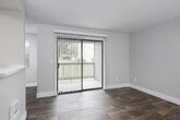 This single-floor unit is designed with a practical, open layout that maximizes living space. The main living area is a standout feature, anchored by a fireplace and finished with durable wood-look plank flooring that extends throughout. Neutral-toned walls and textured ceilings create a clean, understated aesthetic. A pass-through window connects the living space to the kitchen, maintaining an open feel while defining each area. The kitchen is well-equipped, featuring white shaker-style cabinetry with brushed nickel hardware, light stone-look countertops, stainless steel appliances including an electric range and refrigerator, and a skylight-style overhead fixture that brightens the galley-style layout. A pantry closet adds practical storage. The bedrooms are generously sized, each with wood-look flooring, baseboard heating, and windows fitted with blinds that allow natural light. One bedroom includes a walk-in closet with dual hanging rods. The bathroom is appointed with a full soaking tub and shower combination with clean white surround panels and chrome fixtures. A private balcony accessible from the living area provides an outdoor retreat with views of surrounding greenery.