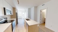 Located in the vibrant Marda Loop neighborhood of Calgary, this well-appointed one-bedroom, two-bathroom unit offers a thoughtfully designed open-concept layout finished with light hardwood flooring and crisp white walls throughout. The modern kitchen is a standout feature, showcasing a long waterfall-edge island with a double undermount sink, warm wood cabinetry paired with upper white cabinets, a subway tile backsplash, and a full suite of stainless steel appliances including a refrigerator, electric range, and microwave. A sleek track light fixture adds a contemporary touch overhead. The kitchen flows seamlessly into the living area, which benefits from a large window that allows ample natural light to fill the space and offers views of the surrounding Calgary skyline and treetops. The bedroom is a serene, minimalist retreat with clean white walls, light hardwood flooring, a baseboard heater, and a bright window framing pleasant outdoor views. The bathroom is finished in a clean, modern style featuring a soaker tub with shower, a wood-toned vanity, and a white countertop. The overall aesthetic is bright, contemporary, and efficiently designed, making excellent use of every square foot.