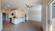 This single-story residence offers a well-designed, open-concept layout that seamlessly connects the kitchen and living area. The kitchen is outfitted with crisp white shaker-style cabinetry, granite countertops, and a full suite of stainless steel appliances, including a range, microwave, and refrigerator. Pendant lighting hangs above the peninsula, which provides added counter space and a natural division between the kitchen and the living area. Wood-look plank flooring runs consistently throughout the space, contributing to a cohesive, modern aesthetic.

The living area is generously proportioned, featuring a ceiling fan and neutral-toned walls that create a bright, airy atmosphere. A sliding glass door leads to a private balcony, allowing natural light to fill the room and offering outdoor access.

The bathroom is well-appointed with white cabinetry, granite countertops, a single-sink vanity with modern fixtures, a large mirror, and a soaking tub with a tiled surround. Wood-look flooring continues into the bathroom, maintaining design consistency. A window in the bathroom provides natural light. Overall, the space presents a clean, contemporary finish with functional and stylish details throughout.