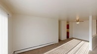 This single-floor residential unit offers a straightforward and functional layout designed for comfortable everyday living. The open living area is finished with neutral wall-to-wall carpeting and features baseboard heating along the perimeter, ensuring warmth throughout. A sliding glass door floods the main living space with natural light and provides access to an outdoor area, while vertical blinds offer privacy and light control.

The kitchen is efficiently appointed with warm oak cabinetry, both upper and lower, paired with light countertops and a double stainless steel sink. Tile flooring and a range complete the practical cooking space, which connects conveniently to the living area via a pass-through opening.

The bedrooms are bright and well-proportioned, each featuring plush carpeting, white horizontal blinds on the windows, and baseboard heating. One bedroom includes a wall-mounted air conditioning unit for year-round climate control.

A generously sized walk-in closet provides ample storage with dual hanging rods and built-in shelving. The bathroom features a tub-shower combination with white tile surround, a toilet, and a vanity with storage, all finished in light, neutral tones. Throughout the unit, the clean white walls and consistent flooring choices create a cohesive and move-in-ready environment.
