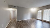 Located at 3621 Wynn Dr in Edmond, Oklahoma, this single-floor unit offers a well-organized layout designed for comfortable, everyday living. Throughout the space, wood-look laminate flooring in warm, natural tones provides a cohesive aesthetic, complemented by neutral gray walls and clean white trim.

The open living area is a highlight of the unit, featuring a textured ceiling, recessed HVAC venting, and a large window with blinds that allows generous natural light to fill the room. French doors in one of the living spaces further enhance the brightness and provide access to the outdoors.

The kitchen is functionally equipped with white cabinetry, stone-toned countertops, and black appliances including a range and dishwasher. Light-toned flooring in the kitchen contrasts subtly with the rest of the unit, adding visual interest.

A hallway connects the main living areas to the private rooms, one of which features a ceiling fan with a light fixture and darker wood-look flooring. Built-in shelving is visible near the kitchen area, offering practical storage. A fire extinguisher is mounted in the corridor, reflecting attention to safety.

The bathroom includes a full tub and shower combo, a white vanity with storage, and durable, easy-to-clean flooring. Overall, the unit presents a clean, move-in-ready environment with consistent finishes throughout.