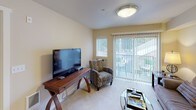 Located at 12710 N Mill Rd in Spokane, Washington, Unit 113 is a thoughtfully laid-out single-floor residence that offers a comfortable and functional living environment. The bedroom is a relaxing retreat, featuring plush carpeting, warm neutral-toned walls, and a large window with vertical blinds that allows natural light to filter in while providing a view of the surrounding greenery. The room offers ample space for furnishings and storage. The living area is equally inviting, with soft carpeting underfoot and a sliding glass door that opens to a private patio, bringing in natural light and outdoor views. This space is well-suited for both relaxing and entertaining. The kitchen is efficiently designed with warm-toned wood cabinetry, light countertops, and durable hardwood-style flooring. It is equipped with a full suite of white appliances, including a refrigerator, electric range, dishwasher, and over-the-range microwave. A dining area adjacent to the kitchen provides a convenient space for meals. A bathroom with cabinetry and vanity lighting is accessible from the kitchen area, adding to the unit's practical layout. The overall design is clean and cohesive, with neutral finishes throughout that create a warm and welcoming atmosphere.