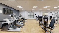 Located at 4125 Chestnut St in Philadelphia's University City neighborhood, this fitness center offers a comprehensive, single-floor workout facility designed to accommodate a wide range of training needs. The space features light hardwood-style flooring throughout, a drop ceiling with recessed panel lighting that ensures bright, even illumination across the entire floor.

The strength training area is well-appointed with a full rack of dumbbells, multiple barbell stations with weight plates, and a variety of Instinct-brand selectorized cable and resistance machines suited for both upper and lower body training. Sturdy support columns are incorporated into the layout without obstructing movement between equipment zones.

The cardio section lines one wall with a row of elliptical trainers, StairMaster steppers, and stationary bikes, providing ample options for aerobic conditioning. Large frosted-glass interior windows add visual openness to this section of the facility.

One of the most distinctive features of the space is the bold, large-scale graffiti-style mural that wraps across the accent walls, injecting vibrant color and urban energy into the environment. Mirrors are strategically placed to expand the sense of space and support form monitoring during workouts.

Overall, the facility presents a dynamic, motivating atmosphere that balances functional equipment density with an energetic aesthetic, making it a well-rounded destination for fitness enthusiasts.