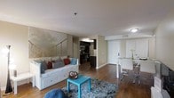 This well-appointed single-floor space offers a thoughtfully designed open-concept layout that seamlessly connects the living, dining, and kitchen areas. The living area is anchored by rich hardwood flooring and features a comfortable daybed-style sofa accented with colorful throw pillows, a plush area rug, and a vibrant teal accent table that adds a pop of color to the neutral palette. A large artistic mural on the living room wall serves as a striking focal point, lending character and depth to the space.

The kitchen is outfitted with dark cabinetry, stainless steel appliances — including a microwave, range, and refrigerator — and ample counter space, making it both functional and stylish. Pendant lighting above the kitchen area enhances the modern aesthetic.

Adjacent to the living space, the dining area accommodates a sleek table with modern chairs, ideal for everyday meals or entertaining. The overall color scheme of warm beige tones, dark finishes, and bright accents creates a balanced and inviting atmosphere. Recessed lighting and flush-mount fixtures provide consistent illumination throughout, while the clean, neutral walls offer a versatile backdrop for personalization.