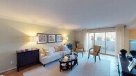 This single-floor residence offers a thoughtfully designed layout with a seamless flow between living, dining, and sleeping areas. The living room is bright and welcoming, featuring crown molding, soft neutral walls, and large sliding glass doors that open to an outdoor balcony, flooding the space with natural light and views of surrounding greenery. A glass-topped oval coffee table and plush seating complete the relaxed yet refined atmosphere.

The dining area accommodates a round glass-top table beneath a pendant light fixture, with corner windows dressed in sheer curtains that invite natural light. A dark wood sideboard with an oval mirror adds an elegant finishing touch.

The kitchen is well-equipped with rich wood cabinetry, granite countertops, and a full suite of stainless steel appliances including a gas range, built-in microwave, dishwasher, and refrigerator.

The primary bedroom is generously sized, offering ample space for a king bed, a seating nook, and a large dresser. It connects to an en-suite bathroom featuring a standalone shower. A second bedroom is equally spacious, with a second full bathroom featuring a soaking tub and classic white tile. Warm tile flooring runs throughout, tying the residence together in a cohesive, comfortable style.