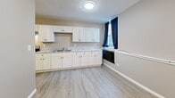 Located at 7 North Park Place in Painesville, Ohio, this thoughtfully designed single-floor unit makes excellent use of its intimate footprint. The kitchen is a standout feature, outfitted with crisp white shaker-style cabinetry, granite-look countertops, a stainless steel refrigerator, and a stainless steel electric range with an under-cabinet range hood. Light wood-look vinyl plank flooring runs throughout, lending a clean, cohesive aesthetic. A window dressed with navy blue curtains brings in natural light and adds a touch of color to the space. A classic cast-iron radiator provides character alongside modern updates.

The unit includes two bathrooms, offering added convenience. One bathroom features marble-look tile flooring and an over-the-toilet storage unit for maximizing space efficiency. The second bathroom area includes a walk-in shower stall and continues the same light flooring found throughout the unit. Neutral taupe and gray wall tones create a calm, understated atmosphere throughout the space.

The overall layout, visible in the dollhouse view, is straightforward and functional, with clearly defined areas for the kitchen, hallways, and bathrooms. The warm-toned entry door adds a welcoming architectural detail. This unit is a well-appointed and practical space in a convenient Painesville location.