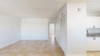 Located in Deerfield Beach, Florida, this single-floor, 2-bedroom, 1-bathroom unit offers a practical and well-maintained layout. Light beige ceramic tile flooring runs consistently throughout the entire space, complemented by crisp white walls and textured ceilings that create a clean, cohesive aesthetic.

The kitchen is a functional highlight, featuring white shaker-style cabinetry, granite-look countertops, stainless steel appliances including a refrigerator and electric range, and a skylight-style overhead fixture that brightens the space. A louvered closet door adjacent to the kitchen provides convenient storage access. The kitchen flows into the combined living area, which offers an open and airy feel with ample natural light from a window fitted with horizontal blinds.

Both bedrooms are well-proportioned, with the primary bedroom offering generous space. Each room features windows with blinds allowing natural light to filter in. One bedroom includes a sliding double-panel closet with paneled doors for organized storage. A dedicated hallway closet provides additional storage.

The bathroom is finished in an all-white palette, featuring a full tub-shower combination with white tile surround, and modern matte black hardware and fixtures, adding a contemporary contrast to the otherwise neutral interior.
