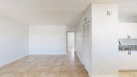 Located in Deerfield Beach, Florida, this single-floor, 2-bedroom, 1-bathroom unit offers a practical and well-maintained layout. Light beige ceramic tile flooring runs consistently throughout the entire space, complemented by crisp white walls and textured ceilings that create a clean, cohesive aesthetic.

The kitchen is a functional highlight, featuring white shaker-style cabinetry, granite-look countertops, stainless steel appliances including a refrigerator and electric range, and a skylight-style overhead fixture that brightens the space. A louvered closet door adjacent to the kitchen provides convenient storage access. The kitchen flows into the combined living area, which offers an open and airy feel with ample natural light from a window fitted with horizontal blinds.

Both bedrooms are well-proportioned, with the primary bedroom offering generous space. Each room features windows with blinds allowing natural light to filter in. One bedroom includes a sliding double-panel closet with paneled doors for organized storage. A dedicated hallway closet provides additional storage.

The bathroom is finished in an all-white palette, featuring a full tub-shower combination with white tile surround, and modern matte black hardware and fixtures, adding a contemporary contrast to the otherwise neutral interior.