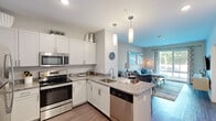 Located at 254 Lynnway in Lynn, Massachusetts, this single-floor residence offers a thoughtfully designed open-concept layout with modern finishes throughout. The kitchen is a standout feature, outfitted with crisp white shaker cabinetry, granite countertops, a full suite of stainless steel appliances — including a refrigerator, range, microwave, and dishwasher — and stylish pendant lighting above a functional peninsula that flows seamlessly into the living area. The living room is bright and welcoming, with large windows that invite natural light and views of the surrounding greenery, complemented by track lighting and warm, neutral tones. The bedrooms are serene and comfortable, each featuring plush carpeting, generous windows with views of lush outdoor scenery, and ample space for furnishings. The bathroom is finished with granite countertops, a wide vanity with an undermount sink, a large mirror, and soft blue walls that create a calm, spa-like atmosphere. Wood-look flooring runs throughout the main living areas, tying the space together with a clean, contemporary aesthetic. The overall ambiance is modern, light-filled, and cohesive.