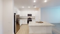 Located on Rollerton Road in Charlotte's 28205 zip code, this single-floor unit offers a clean, modern interior designed for comfortable everyday living. The open-concept layout connects the living area to the kitchen seamlessly, with light hardwood flooring running throughout and ceiling fans providing both style and function.

The kitchen is a standout feature, equipped with stainless steel appliances including a refrigerator, range with microwave, and dishwasher. Crisp white cabinetry extends to the ceiling, offering generous storage, while granite countertops add a polished finish. A central kitchen island with a double stainless steel sink and additional granite surface provides both prep space and a natural gathering point.

The living area is bright and open, benefiting from multiple windows fitted with blinds that allow natural light to fill the room. Recessed lighting complements the ceiling fans throughout the space.

The bathroom is well-appointed with a granite-topped vanity, white cabinetry, brushed nickel hardware, a full-size soaking tub with shower, and hardwood-style flooring that carries the home's consistent aesthetic. The layout, as visible in the dollhouse overview, is efficiently organized with easy flow between all areas, making this a practical and attractive single-level space in Charlotte.