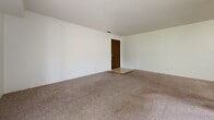 Located at 215 E Arbor Ave in Bismarck, North Dakota, this single-floor unit offers four bedrooms, one full bathroom, and a practical layout designed to maximize livable space. The primary bedroom is generously proportioned, providing ample room for a full furniture arrangement, and features a walk-in closet with built-in shelving and hanging rods for organized storage. Additional bedrooms are carpeted and well-lit, each offering windows that bring in natural light and views of the surrounding greenery. A second walk-in closet adds further storage convenience throughout the unit. The full bathroom is outfitted with a warm wood-toned vanity with dual sinks, a large mirror, tiled flooring, and a full-size tub and shower combination with built-in shelving. The open living area is spacious and carpeted, flowing from the hallway toward the balcony access point. The private balcony, enclosed by a black metal railing, overlooks a lush, tree-lined outdoor area, offering a peaceful outdoor retreat. The kitchen area, visible in the floor plan, connects fluidly to the main living space. Throughout the unit, neutral tones, textured ceilings, and consistent carpeting create a cohesive, understated aesthetic suited for comfortable everyday living.