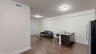 This single-floor unit offers a practical and modern layout across three bedrooms and three bathrooms. The open-concept living and kitchen area serves as the heart of the unit, featuring rich hardwood-style flooring that extends throughout the common spaces. The kitchen is well-appointed with stainless steel appliances — including a full-size refrigerator, range, and microwave — complemented by dark espresso cabinetry, granite countertops, and a peninsula with bar seating that doubles as a casual dining space. The living area provides a comfortable, open setting with clean white walls and flush ceiling lighting.

The three bedrooms offer a calm, neutral aesthetic with plush carpeting, white trim, and windows fitted with blinds that allow for natural light while maintaining privacy. The primary bedroom includes access to additional closet or utility space. Each of the three bathrooms is finished with floor-to-ceiling tile, a glass-enclosed walk-in shower, a wall-mounted vanity with a white basin sink, and a well-lit mirror — delivering a clean, contemporary feel. Throughout the unit, the consistent use of neutral tones, modern fixtures, and quality materials creates a cohesive and functional living environment suited for multiple occupants.