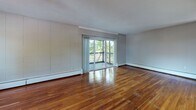 Located at 444 Meshanticut Valley Pkwy in Cranston, Rhode Island, this single-floor residence offers a well-organized and functional layout across its living spaces. The open living and dining area is a standout feature, showcasing rich, polished hardwood flooring that extends throughout and a large sliding glass door that opens onto a private balcony, filling the space with natural light and offering pleasant views of the surrounding greenery. A pass-through window connects the living area to the kitchen, enhancing the open feel of the space.

The kitchen is thoughtfully appointed with warm-toned wood cabinetry, granite countertops, tile flooring, and a full suite of white appliances including an electric range and dishwasher. A window above the sink brings in additional natural light.

The bedrooms are carpeted for comfort and feature panel-style wall detailing, individual windows with outdoor views, and baseboard heating. One bedroom also includes a wall-mounted air conditioning unit for year-round climate control.

The bathroom is clean and well-finished, featuring a granite-topped white vanity, a framed mirror with overhead lighting, tile flooring, and a shower-tub combination with a decorative curtain. The overall aesthetic of the residence is practical and comfortable, offering a cohesive and livable environment.