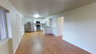 This single-floor space showcases a clean, modern design with an open-concept layout that seamlessly connects the kitchen and living area. The kitchen is outfitted with white cabinetry, a peninsular countertop, and stainless steel appliances, including a refrigerator, range, and over-the-range microwave. A sink is positioned along the peninsula, adding both functionality and a natural dividing point between the kitchen and the open living space. The flooring throughout is a warm, light-toned hardwood-style material that lends consistency and brightness across the entire space. Walls are finished in a neutral white and light gray palette, contributing to the unit's airy, clean aesthetic. A closet with a bifold door is accessible just off the kitchen area, providing additional storage. The living area is generously proportioned, offering flexibility for a variety of furniture arrangements. Overall, the space presents a practical and well-maintained interior with modern finishes, making it a functional and inviting single-floor living environment.