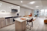 Located on the 10th floor at 20 George St in downtown Hamilton, Ontario, this contemporary condominium offers 910 square feet of thoughtfully designed living space across a single level. The open-concept layout connects the kitchen, living, and dining areas seamlessly, all finished with light wood-look luxury vinyl flooring throughout. The modern kitchen features two-tone cabinetry — warm wood lower cabinets paired with high-gloss white uppers — complemented by quartz countertops, a subway tile backsplash, a central island with seating, and a full suite of stainless steel appliances including a built-in oven, electric cooktop, dishwasher, and over-the-range microwave. The bright living and dining areas are framed by expansive floor-to-ceiling windows and a corner window arrangement, flooding the space with natural light and offering sweeping views of the Hamilton skyline. Two well-proportioned bedrooms feature large windows, light neutral walls, and built-in sliding door closets. The unit includes two bathrooms: a full bath with a soaker tub and shower combination, and a second bathroom with a glass-enclosed walk-in shower. Clean lines, neutral tones, and contemporary finishes define the overall aesthetic of this modern urban residence.
