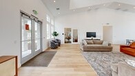 Located at 6497 W Mount Fremont Dr in Herriman, Utah, this single-floor community space offers a generously sized, open layout designed for both comfort and functionality. The interior is defined by soaring vaulted ceilings that amplify the sense of openness throughout, while light hardwood flooring runs seamlessly across the entire space, contributing to its clean, modern aesthetic.

The main living area serves as the heart of the space, featuring large floor-to-ceiling windows and glass double entry doors that flood the interior with natural light and provide clear views of the surrounding community and pool area. A comfortable seating arrangement with a sofa and accent chairs creates a welcoming lounge atmosphere.

The combined dining area is equipped with multiple round tables and seating, making it well-suited for gatherings and group activities. Expansive windows frame views of the neighboring residential buildings and outdoor amenities, further enhancing the bright, airy ambiance.

A private office, enclosed by glass-paneled sliding doors, offers a dedicated workspace that remains visually connected to the main area while providing a quiet, functional retreat. The crisp white walls throughout complement the natural light and contribute to a fresh, contemporary feel. Overall, this thoughtfully designed space balances open communal areas with purposeful private zones.