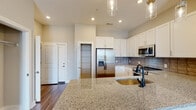 Located at 1841 Dusty Miller Lane in Wilmington, NC, this single-floor residence offers a well-designed layout with contemporary finishes throughout. The kitchen is a standout feature, showcasing an expansive granite island with an undermount sink, crisp white shaker cabinetry, a textured tile backsplash, and a full suite of stainless steel appliances including a French door refrigerator, range, and built-in microwave. Pendant lighting above the island adds a refined touch to the open, airy space. Wood-look flooring runs through the main living and kitchen areas, providing a warm, cohesive aesthetic. The primary bathroom is generously proportioned, featuring dual undermount sinks set in granite countertops, a glass-enclosed walk-in shower with tile surround, and direct access to a spacious walk-in closet equipped with wire shelving on multiple levels. A secondary bathroom includes a tub-shower combination with subway tile, a granite vanity top, and matching wood-look flooring. The dedicated laundry area accommodates a full-size washer and dryer side by side with overhead shelving. Bedrooms are carpeted for comfort, with elevated ceilings that enhance the sense of openness. An outdoor covered area with wood-beam ceiling detail is also visible, offering additional living space.