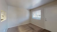 This single-floor residence offers a straightforward and practical layout designed for efficient everyday living. The open living area is finished with wall-to-wall carpet in a warm neutral tone, creating a comfortable and inviting atmosphere. A window fitted with horizontal blinds allows natural light to fill the space while maintaining privacy. The living area connects seamlessly to the kitchen via a pass-through opening, enhancing the sense of flow between spaces.

The galley-style kitchen is well-appointed with crisp white cabinetry offering ample storage, dark granite-style laminate countertops, and wood-look luxury vinyl plank flooring. Black appliances, including a range, refrigerator, and dishwasher, provide a bold contrast against the light cabinetry and neutral walls.

The bedroom is generously proportioned with plush carpeting and a window that brings in natural light, providing a calm and restful retreat. Clean white walls and simple finishes keep the room feeling bright and open.

The full bathroom features a combined tub and shower with a white surround, a white vanity with a granite-style countertop and undermount sink, and wood-look flooring that ties the space together. A large mirror above the vanity enhances the sense of space. Overall, the residence presents a clean, move-in-ready aesthetic with consistent finishes throughout.