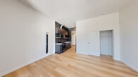 Located in Portland's vibrant Northwest District, this modern studio unit at 1126 NW 18th Ave offers a thoughtfully designed single-floor layout with a clean, contemporary aesthetic throughout. Light-toned hardwood flooring runs seamlessly across the entire space, complementing the crisp white walls and creating a bright, cohesive atmosphere.

The open main area serves as both living and sleeping space, featuring recessed lighting, a built-in closet with sliding door, and a wall-mounted utility panel. Natural light enters through a window visible from the main living zone, adding warmth to the minimalist interior.

The kitchen is a standout feature, finished in bold matte dark cabinetry with gold hardware accents. It is equipped with stainless steel appliances including an electric range, over-the-range microwave, and a refrigerator. A stainless steel sink with a matte black faucet and light-toned countertops complete the functional yet stylish cooking area. An exposed ventilation duct adds an industrial touch.

The bathroom is clean and modern, featuring a wood-toned vanity with white countertop, gold hardware, a large mirror, tiled walk-in shower, and in-unit stacked Samsung washer and dryer — a highly practical inclusion. Overall, the unit presents a well-appointed, efficient living space with modern finishes throughout.