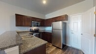 This thoughtfully designed 3-floor residence offers a functional and stylish layout spread across multiple levels, connected by a prominent staircase visible in the architectural overview. The kitchen is a standout feature, outfitted with rich dark cabinetry, granite countertops, a full suite of stainless steel appliances including a refrigerator, range, and over-the-range microwave, and durable wood-style flooring. A raised breakfast bar peninsula provides a natural divide between the kitchen and the adjacent living area, adding both practicality and visual interest. The bathrooms are finished to a high standard, featuring large-format stone-look tile work throughout the walk-in shower, a granite-topped vanity, and chrome fixtures that lend a clean, polished aesthetic. The bedrooms are generously proportioned, carpeted for comfort, and benefit from multiple windows dressed with vertical blinds that allow for natural light while maintaining privacy. A lower-level room features wood-style flooring, neutral walls, and a window that brings in additional natural light, offering flexible use as a recreation room or additional living space. Throughout the residence, neutral tones, clean lines, and consistent finishes create a cohesive and welcoming ambiance across all three floors.