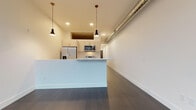Located at 1125 N 9th St in Milwaukee, Wisconsin, this contemporary single-floor unit offers a thoughtfully designed open-concept layout with a clean, modern aesthetic throughout. The living area is expansive and bright, featuring dark hardwood flooring that extends seamlessly through the space, complemented by crisp white walls that enhance the sense of openness.

The kitchen is a standout feature, equipped with a full suite of stainless steel appliances including a refrigerator with ice maker, electric range, over-the-range microwave, and dishwasher. Light-toned cabinetry and white countertops provide a sleek contrast to the dark hardware and flooring, while a peninsula with pendant lighting above serves as both a functional workspace and a casual dining area. An exposed metal duct running along the upper wall adds an industrial loft-like character to the space.

The bedroom receives generous natural light through large floor-to-ceiling windows that frame views of the surrounding Milwaukee streetscape. The bathroom is finished in a minimalist style, featuring a dark-toned vanity with a white countertop and undermount sink, a large mirror, light tile flooring, and a tub-shower combination with chrome fixtures. Together, the rooms create a cohesive, modern living environment well-suited for urban living in Milwaukee.