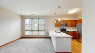 Located at 1868 N Astor St in Milwaukee's vibrant lower east side, this well-appointed one-bedroom, one-bathroom unit offers a thoughtfully designed single-floor layout. The kitchen serves as a central highlight, featuring warm medium-toned wood cabinetry, gleaming white countertops, and a full suite of stainless steel appliances including a range, built-in microwave, refrigerator, and dishwasher. A peninsula with an integrated sink and pendant lighting above creates an open, functional workspace that connects naturally to the living area. Light wood flooring in the kitchen transitions to plush carpeting in the main living space and bedroom. The living area benefits from natural light through a glass-panel exterior door that opens to a private balcony, offering views of the surrounding Milwaukee neighborhood and tree canopy. The comfortably sized bedroom includes two windows for additional natural light and direct access to a walk-in closet. The bathroom is finished with matching wood-toned cabinetry, a white countertop vanity, a large mirror, and a full tub/shower combination. Neutral wall tones and warm wood trim throughout lend the space a cohesive, welcoming ambiance.