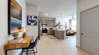 This single-floor residence is designed with a contemporary aesthetic, combining functionality and style across its well-planned layout. Light wood-style flooring flows consistently throughout the space, creating a cohesive and airy feel.

The open-concept kitchen seamlessly connects to the living area, making it ideal for everyday living and entertaining. The kitchen is outfitted with gray cabinetry, a white countertop peninsula with an undermount sink, stainless steel appliances including a refrigerator, range, and microwave, and a white subway tile backsplash. Pendant lighting above the peninsula adds a refined touch.

The living area is bright and welcoming, featuring a ceiling fan, natural light from large windows with blinds, and enough room for comfortable seating arrangements. Adjacent to the entry, a dedicated workspace or console area provides additional functional space.

The primary bedroom is generously sized, accommodating a full bed with room to spare, and benefits from natural light through large windows. It includes access to a spacious walk-in closet outfitted with wire shelving systems and ample hanging space. A second bedroom offers similar scale and storage. The full bathroom features a tub-shower combination with gray cabinetry and matching countertops, consistent with the home's overall palette.