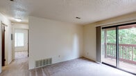 Located at 3110 S Jefferson Ave in Springfield, Missouri, this single-floor unit offers a straightforward and functional layout suitable for everyday living. The open living area features neutral wall-to-wall carpeting and a textured ceiling, creating a clean and simple aesthetic. A sliding glass door provides direct access to a wood-decked balcony that overlooks mature trees, bringing in natural light and a pleasant outdoor connection. The galley-style kitchen is positioned adjacent to the living space and is well-equipped with dark wood cabinetry providing ample storage both above and below the counters, a white gas range with overhead ventilation, a full-size refrigerator, and a double-basin sink. Tile flooring runs throughout the kitchen, offering easy maintenance. The bedroom is a comfortably sized, carpeted room with a window fitted with blinds that allow for natural light and privacy. The full bathroom features tile flooring, a vanity with a dark wood cabinet, and a full tub-shower combination with a clean white surround. Throughout the unit, a consistent neutral color palette and textured ceilings contribute to a cohesive, understated atmosphere.