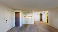 This single-story unit offers a practical and functional layout across a comfortable footprint. The living area is carpeted and open in feel, featuring a ceiling fan and a pass-through opening that connects to the kitchen, allowing for easy interaction between spaces. Neutral-toned walls and textured ceilings are consistent throughout, contributing to a uniform aesthetic.

The galley-style kitchen is efficiently arranged with wood-toned cabinetry lining both sides, providing ample upper and lower storage. Light-colored countertops, a white electric range, dishwasher, and a sink with under-cabinet storage complete the kitchen's functional design. Tile flooring runs through this space.

A hallway connects the main living area to both bedrooms and the bathroom. The primary bedroom is a well-proportioned space featuring carpet, a window with outdoor views, and access to two closets—one standard and one walk-in with built-in shelving. The second bedroom is carpeted and also features a window with natural light. The bathroom includes a wood-cabinet vanity with a wide mirror, a lighted fixture above, and tile flooring.