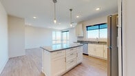 Located in Elkhorn, Nebraska, this well-appointed 2-bedroom, 2-bathroom residence offers a thoughtfully designed single-floor layout with a clean, modern aesthetic. The open-concept kitchen and living area serves as the heart of the home, showcasing white shaker cabinetry, granite countertops, and a full suite of stainless steel appliances including a refrigerator, range, microwave, and dishwasher. A central kitchen island with matching granite provides additional prep space and casual seating, while dual pendant lights with brass accents add a stylish touch overhead. Recessed lighting and large windows allow abundant natural light to fill the space, offering open views of the surrounding Elkhorn landscape. Light-toned hardwood-style flooring runs throughout the main living areas, lending a warm and cohesive feel. The spacious primary bedroom features plush carpeting, a dedicated closet, and direct access to its own bathroom. The second bedroom is equally well-sized with soft carpet and generous closet space. Both bathrooms are finished with granite vanity tops and clean, neutral tiling. The layout also includes two closets for ample storage. Overall, the space presents a bright, modern, and functional living environment suited for comfortable everyday living.