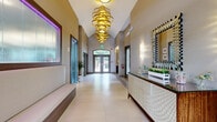 Located at 40 East Hanover Avenue in Morris Plains, NJ, this single-story clubhouse delivers a polished and welcoming environment for residents. The space is thoughtfully organized across a compact yet efficient footprint, encompassing a grand entrance lobby, a fitness center, and additional support areas.

The entrance lobby immediately impresses with its soaring vaulted ceiling and large-format porcelain tile flooring that reflects natural light streaming through the glass-paneled double entry doors, accented by a transom window above. Two striking gold spiral chandeliers serve as dramatic focal points, casting warm light throughout the corridor. Built-in seating with upholstered cushions lines one wall, while a textured mosaic credenza and a bold geometric mirror add refined decorative touches. Subtle ambient lighting, including colorful accent panels, contributes to a vibrant yet sophisticated atmosphere.

The fitness center is generously outfitted with a comprehensive range of equipment, including strength-training machines, free weights, cardio machines such as ellipticals and a StairMaster, and flat bench stations. Floor-to-ceiling mirrors expand the sense of space, while large windows allow natural light to flood in, creating an energizing workout environment. The durable resilient flooring is well-suited for active use. Together, these spaces establish the clubhouse as a functional and aesthetically elevated amenity hub.