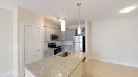 Located at 3860 Danbrook Rd in Burlington, NC, this single-floor residence offers a thoughtfully designed layout with modern finishes and a bright, neutral color palette. The kitchen serves as a central highlight, showcasing granite countertops, gray shaker-style cabinetry, a subway tile backsplash, and a full suite of stainless steel appliances including an electric range, built-in microwave, and refrigerator. A peninsula with an undermount sink and pendant lighting above provides additional prep space and a natural gathering point that connects the kitchen to the open living area. The living space features light wood-style flooring that flows seamlessly throughout, creating a clean and cohesive look. The bedroom is carpeted for added comfort and includes a ceiling fan with light fixture, contributing to a relaxed atmosphere. The bathroom is finished with matching granite countertops, gray cabinetry, an undermount sink, a framed mirror, and light flooring that complements the rest of the home. Clean white trim and soft neutral wall tones are consistent throughout, lending the space a fresh, move-in-ready feel. The overall design balances modern functionality with understated elegance, making it a comfortable and practical living environment.