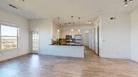 Located along TPC Pkwy in San Antonio, TX, this two-bedroom, one-bathroom residence offers a well-designed single-floor layout with a clean, modern aesthetic throughout. The open-concept kitchen and living area serves as the heart of the home, featuring a central kitchen island with a dark granite countertop, white cabinetry, olive-toned tile backsplash, stainless steel appliances, and elegant pendant lighting overhead. Wood-look tile flooring runs seamlessly throughout the space, adding warmth and cohesion. The living area is bright and airy, with large windows that frame scenic views of the surrounding Texas Hill Country landscape and access to an outdoor area via a glass-panel door. Both bedrooms are comfortably sized, filled with natural light from multiple windows, and include ceiling fans. The primary bedroom connects conveniently to the bathroom and a walk-in closet, which is equipped with multiple hanging rods and shelving for ample storage. The bathroom continues the home's refined aesthetic with dark granite countertops, white cabinetry, mosaic tile accents, and a vessel sink. Throughout the residence, crisp white walls and consistent flooring create a bright, cohesive living environment.