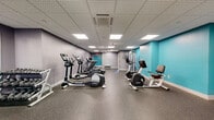 Located at 294 Main St in Hartford, Connecticut, this single-floor fitness facility offers a thoughtfully designed layout dedicated to health and wellness. The space is organized across two primary areas connected by hallways that guide occupants through the facility with ease.

The main exercise room is a generously sized, well-lit space featuring a dropped ceiling with recessed and panel lighting that evenly illuminates the room. The durable speckled rubber flooring provides cushioning underfoot, while the room is equipped with a comprehensive selection of cardio and strength machines, including treadmills, ellipticals, stationary bikes, and cable weight machines. Vivid teal accent walls add an energizing pop of color to the space.

An adjoining open studio room offers a versatile, open floor plan with light wood-toned flooring and a full-length mirror along one wall. A striking large-scale botanical mural serves as a vibrant focal point, creating a calming atmosphere ideal for yoga, stretching, or group fitness classes. Recessed ceiling lights keep the space bright and inviting.

The accessible bathroom is finished with a combination of white subway tile and large-format decorative tiles featuring a graphic urban print. A wall-mounted sink, round mirror, and stainless grab bars complete this clean, functional space. Together, these rooms create a complete and professional fitness environment.