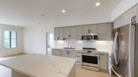 This thoughtfully designed single-floor residence showcases a clean, contemporary aesthetic carried consistently throughout every room. The kitchen serves as a central highlight, featuring soft gray shaker-style cabinetry with matte black hardware, a crisp white subway tile backsplash, and striking quartz countertops with elegant veining. A generous island provides additional prep and gathering space, while a full suite of stainless steel appliances — including a gas range, over-the-range microwave, dishwasher, and French door refrigerator — completes the culinary space. Light wood-tone flooring flows seamlessly through the kitchen and into the adjacent living and bedroom areas, lending warmth and continuity.

The bedrooms are bright and airy, with large windows inviting an abundance of natural light. One bedroom offers sweeping water views, adding a striking outdoor dimension. The primary bathroom is especially spacious, featuring a double-sink vanity with an illuminated mirror, a soaking tub, and a separate glass-enclosed shower. A sizable walk-in closet provides ample storage. A second full bathroom mirrors the same modern finishes, with a quartz-topped vanity and a tub-shower combination. Recessed lighting and white walls throughout create a bright, move-in-ready environment.