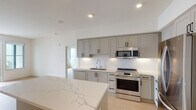 This thoughtfully designed single-floor residence showcases a clean, contemporary aesthetic carried consistently throughout every room. The kitchen serves as a central highlight, featuring soft gray shaker-style cabinetry with matte black hardware, a crisp white subway tile backsplash, and striking quartz countertops with elegant veining. A generous island provides additional prep and gathering space, while a full suite of stainless steel appliances — including a gas range, over-the-range microwave, dishwasher, and French door refrigerator — completes the culinary space. Light wood-tone flooring flows seamlessly through the kitchen and into the adjacent living and bedroom areas, lending warmth and continuity.

The bedrooms are bright and airy, with large windows inviting an abundance of natural light. One bedroom offers sweeping water views, adding a striking outdoor dimension. The primary bathroom is especially spacious, featuring a double-sink vanity with an illuminated mirror, a soaking tub, and a separate glass-enclosed shower. A sizable walk-in closet provides ample storage. A second full bathroom mirrors the same modern finishes, with a quartz-topped vanity and a tub-shower combination. Recessed lighting and white walls throughout create a bright, move-in-ready environment.