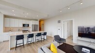 Located in the heart of Chicago's River North neighborhood, this modern residence at 1 W Chicago Ave offers a thoughtfully designed open-concept layout with contemporary finishes and sweeping city skyline views. Light wood-tone flooring runs throughout, creating a cohesive and airy aesthetic across all areas.

The living room serves as the centerpiece of the space, anchored by expansive floor-to-ceiling windows that frame dramatic views of the Chicago skyline and flood the interior with natural light. Track lighting overhead complements the abundant daylight. The living area flows seamlessly into the kitchen, which features a large waterfall-edge island with bar seating, sleek white cabinetry extending to the ceiling, quartz countertops, and stainless steel appliances including a gas range and French door refrigerator.

The bedroom continues the floor-to-ceiling window theme, offering direct city views and an abundance of natural light. The space is bright and serene, with clean white walls and ample room for furnishings.

The bathroom is finished with a wide double vanity topped with white quartz, an illuminated mirror, and a glass-enclosed walk-in shower with a rainfall showerhead. A hallway with in-unit storage connects the private and communal areas, completing this well-appointed urban residence.