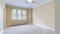 This single-floor unit presents a straightforward and functional layout across several distinct spaces. The main living and bedroom areas are finished with neutral-toned, wall-to-wall carpet, lending a comfortable and quiet underfoot feel. Crown molding runs consistently along the ceilings, adding a traditional architectural detail, while ceiling fans with integrated light fixtures provide both ventilation and ambient lighting. Wide windows dressed with horizontal blinds allow natural light to fill the rooms, offering views of surrounding greenery. Baseboard heating units run along the exterior walls, providing an efficient heating solution throughout the carpeted spaces.

The kitchen is equipped with oak cabinetry above and below the counter, providing ample storage. White appliances, including a range and a full-size refrigerator, are included, and the space features a single basin sink. Light tile flooring grounds the kitchen area practically.

The bathroom includes a combination tub and shower, an oak vanity with a white countertop, a wall-mounted mirror, and white tile detailing along the walls. Light wood-style flooring completes the space. A closet with built-in shelving is accessible off the main hallway, offering dedicated storage within the unit.