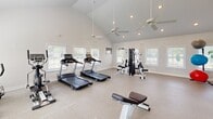 Located at 1032 Mohawk St in Savannah, GA, this single-level exercise room offers a generously sized, purpose-built fitness environment designed to accommodate a comprehensive range of workout activities. The space is defined by its striking vaulted ceilings, which soar to a considerable height and contribute to an open, airy atmosphere that is further enhanced by multiple ceiling fans providing consistent air circulation throughout.

Natural light flows in abundantly through several white-shuttered windows positioned along the walls, creating a bright and motivating environment. The floors are finished with a durable, speckled rubberized surface well-suited for fitness use. A large wall-to-wall mirror along one side of the room visually expands the space and supports proper form during exercise.

The layout comfortably accommodates a variety of equipment, including treadmills, an elliptical, a stationary bike, a multi-station cable machine, a weight bench, a tiered dumbbell rack, medicine ball storage, stability balls, and a BOSU trainer. Recessed lighting supplements the natural light, ensuring the space remains well-lit at all times. A glass-paneled door provides direct access to the exterior, adding convenience and ventilation options.