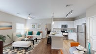 This single-story, 2-bedroom, 2-bathroom residence offers a well-designed open-concept layout that seamlessly connects the main living areas. The living room is bright and welcoming, featuring wood-style flooring, a ceiling fan, and multiple windows that allow natural light to fill the space. A glass-top coffee table and generous seating area make it an inviting environment for both relaxing and entertaining.

The kitchen is a functional highlight of the unit, showcasing white shaker-style cabinetry, granite countertops, and a full suite of stainless steel appliances, including a refrigerator, range, and microwave. A kitchen island with bar seating provides additional prep space and casual dining options, while track lighting overhead ensures excellent task illumination.

Both bedrooms are carpeted and comfortably sized, each equipped with ceiling fans and ample closet space. One bedroom includes a walk-in closet and direct access to a private bathroom featuring a glass-enclosed shower, granite vanity, and tile flooring. The second bathroom offers a shower-tub combination and a similarly appointed granite vanity. Neutral gray wall tones throughout the unit contribute to a cohesive, contemporary aesthetic.