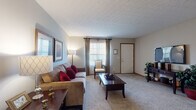 Located at 5222 Flower Valley Dr in Canal Winchester, Ohio, this single-floor residence offers a well-designed layout with comfortable living spaces and practical amenities throughout. The living room is generously proportioned, featuring plush wall-to-wall carpeting, a textured ceiling, and large windows dressed with floor-length drapes that allow ample natural light. The open feel of the room provides flexible furniture arrangements and connects seamlessly to the rest of the home. The galley-style kitchen is efficiently organized with warm oak cabinetry, tile flooring, a double sink, and white appliances including a refrigerator and electric range. Adjacent to the kitchen, the dining area accommodates a round table beneath a pendant light fixture and offers direct access to the in-unit laundry closet, adding everyday convenience. The primary bedroom is spacious, with carpet flooring, a textured ceiling, and a window with curtain panels. A secondary bedroom features a sliding-door closet with a built-in rod, offering practical storage. The full bathroom includes a tub-shower combination, tile flooring, a vanity with storage, and a well-lit mirror. Neutral tones, wood-trimmed doors, and carpeted floors create a cohesive and welcoming atmosphere throughout the home.