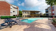 Located at 15035 Westpark Dr in Houston, Texas, this single-story amenity facility offers residents a well-rounded recreational experience combining indoor fitness and outdoor leisure. The building's exterior features a warm yellow facade with a covered upper balcony, large multi-pane windows, and French doors that open directly to the pool area, creating a seamless indoor-outdoor connection.

The fitness center is thoughtfully organized across a comfortable open layout, finished with crown molding, neutral warm-toned walls, and carpet flooring throughout. Large windows flood the space with natural light while offering views of the outdoor pool, creating an inviting workout environment. The gym is equipped with cardio machines including Matrix treadmills and a Life Fitness elliptical trainer, as well as a multi-station cable weight machine to support a full-body workout routine. Motivational fitness posters and a community bulletin board add a welcoming, community-oriented touch.

French doors within the fitness area provide direct access to the outdoor pool deck, reinforcing the connection between indoor and outdoor amenities. The expansive pool area features a sparkling rectangular swimming pool surrounded by a stamped concrete deck, furnished with lounge chairs for relaxation. Mature landscaping and a covered balcony overlooking the pool complete this inviting outdoor retreat.
