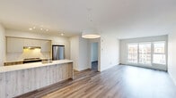 Located at 308 Rue Crevier in Saint-Laurent, this well-designed 2-bedroom, 1-bathroom unit offers a clean, modern aesthetic throughout. Light-toned laminate flooring flows consistently across all rooms, complementing the crisp white walls and creating a bright, cohesive atmosphere.

The open-concept kitchen and living area forms the heart of the unit. The kitchen is outfitted with contemporary two-tone cabinetry — white uppers paired with wood-finish lowers — a stone-look countertop peninsula with an undermount sink, a tile backsplash, stainless steel appliances including a refrigerator and range, and track lighting overhead. A large pendant light marks the transition into the living area, which benefits from a wall-mounted air conditioning unit for year-round comfort.

Both bedrooms are well-proportioned and filled with natural light through large windows offering views of the surrounding neighbourhood. The primary bedroom includes its own closet and wall-mounted AC unit, while a separate dedicated closet space adds additional storage. Baseboard heaters are present in the bedrooms.

The bathroom is finished in a clean, modern style with white tile walls, a combined bathtub and shower enclosed by a glass panel, a white vanity with integrated sink, and dark tile flooring. The unit's overall design is functional, contemporary, and move-in ready.