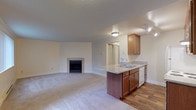 This single-floor residence offers a thoughtfully designed open-concept layout that seamlessly connects the living area and kitchen. The spacious living room is anchored by a tile-surround fireplace, creating a warm focal point, and is finished with plush wall-to-wall carpeting. Large windows and a sliding glass door flood the space with natural light while providing outdoor access.

The kitchen is efficiently arranged with warm medium-tone wood cabinetry, light granite-style countertops, and wood-look flooring. It features a full suite of white appliances — including a refrigerator, electric range, dishwasher, and range hood — along with a peninsula that opens toward the living area, ideal for casual dining or entertaining.

The bedrooms are carpeted and generously sized, each with windows that bring in natural light and baseboard heating. The primary bedroom includes access to a closet and connects to the bathroom.

The bathroom is well-equipped with a wood-look tile floor, a vanity with granite-style countertops and a single sink, and a full bathtub with shower. A notable feature is the stacked in-unit washer and dryer, adding everyday convenience. The textured ceilings and neutral palette throughout give the home a clean, cohesive feel.