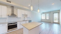 Located at 10 Westedge Street in Charleston's vibrant 29403 zip code, this well-appointed one-bedroom, one-bathroom residence offers a thoughtfully designed open-concept layout with modern finishes throughout. Light wood-look flooring flows seamlessly across the entire space, creating a cohesive and airy feel. The kitchen is a standout feature, showcasing crisp white shaker cabinetry, a herringbone-patterned tile backsplash, quartz countertops, stainless steel appliances including a French door refrigerator, slide-in range, dishwasher, and a stainless wall-mounted range hood. A center island with pendant lighting provides additional prep space and casual seating. The living room benefits from large windows and a glass door leading to a private balcony, inviting generous natural light and exterior views of the Charleston skyline. The bedroom is a comfortable retreat with dual windows, a ceiling fan, and abundant natural light. The walk-in closet features multi-tier wire shelving for organized storage. The bathroom offers a clean, contemporary design with a sliding glass-enclosed walk-in shower and tile flooring. This well-laid-out residence combines modern urban living with the charm of one of South Carolina's most celebrated cities.
