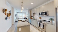 This single-floor residence is designed with a clean, contemporary aesthetic highlighted by an open-concept layout that seamlessly connects the kitchen, dining, and living areas. The kitchen serves as a focal point, featuring granite countertops, a central island with pendant lighting overhead, soft gray cabinetry, a white subway tile backsplash, and a full suite of stainless steel appliances including a gas range, built-in microwave, dishwasher, and refrigerator with ice maker. Light wood-look flooring runs throughout the main living areas, enhancing the bright, airy feel supported by recessed lighting.

The living area flows naturally from the kitchen, benefiting from a large window that invites natural light and frames urban views. The bedroom is a calm, well-lit retreat featuring large windows with sheer curtains, a ceiling fan, and plush carpeting underfoot. An en-suite bathroom offers a granite-topped vanity with ample cabinetry, large-format tile flooring, and direct access to a dedicated walk-in closet equipped with built-in shelving and hanging rods. Throughout the residence, a consistent neutral palette and thoughtful finishes contribute to a cohesive, polished atmosphere.