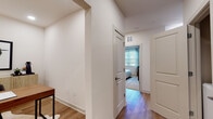 This thoughtfully designed single-floor residence offers a cohesive modern aesthetic defined by warm light wood flooring, crisp white walls, and rich dark wood cabinetry. The open-concept kitchen is a standout feature, boasting an extended island with a deep undermount sink, quartz countertops, stainless steel appliances including a range and built-in microwave, and sleek pendant lighting that illuminates the generous workspace. The living area flows naturally from the kitchen and dining space, offering a bright, inviting atmosphere enhanced by large windows dressed with blinds and sheer curtains that invite natural light. Two well-proportioned bedrooms provide comfortable retreats; the primary bedroom features carpet flooring, a large window with outdoor views, and ample space, while the second bedroom mirrors the same light-filled, serene character. Both bathrooms are finished consistently with dark wood vanities, white quartz countertops, and wood-look flooring — one featuring a soaking tub with shower combination and the other a shower with curtain. A dedicated home office, enclosed and illuminated by recessed lighting, offers a quiet workspace complete with clean white walls and wood flooring. A connecting hallway ties all spaces together efficiently, completing this well-appointed and functional single-level layout.
